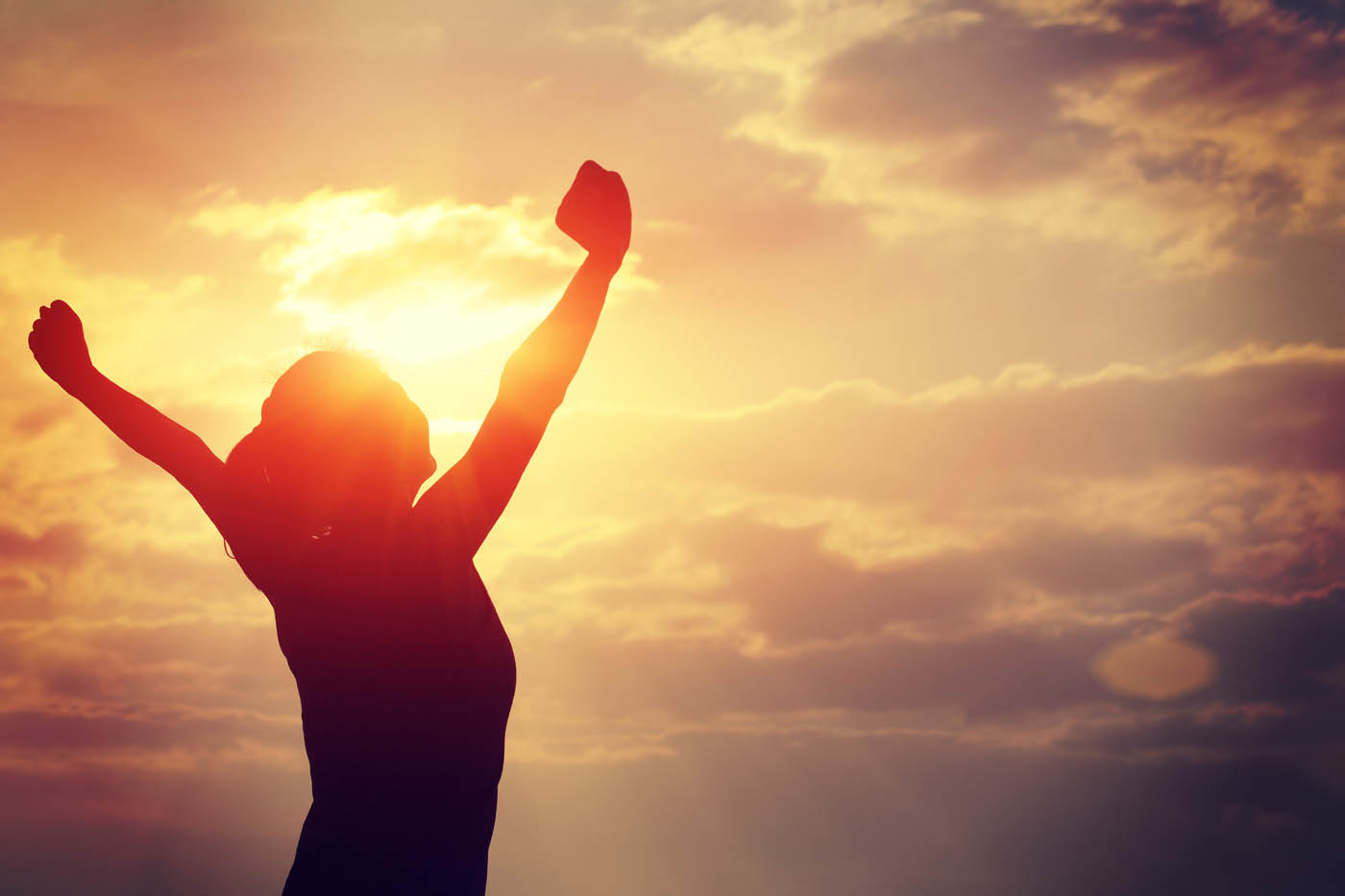A woman standing in the light with her arms up in the air - learn how you can get relief with Light Lounge's back pain management in Holland, MI.