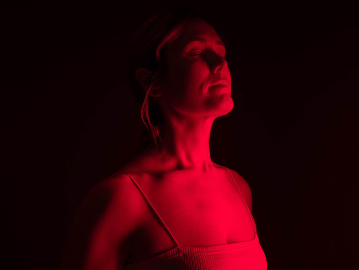 A woman standing in red light - learn about the alternative that Light Lounge brings if you are looking for pain management specialist in Evergreen, CO.