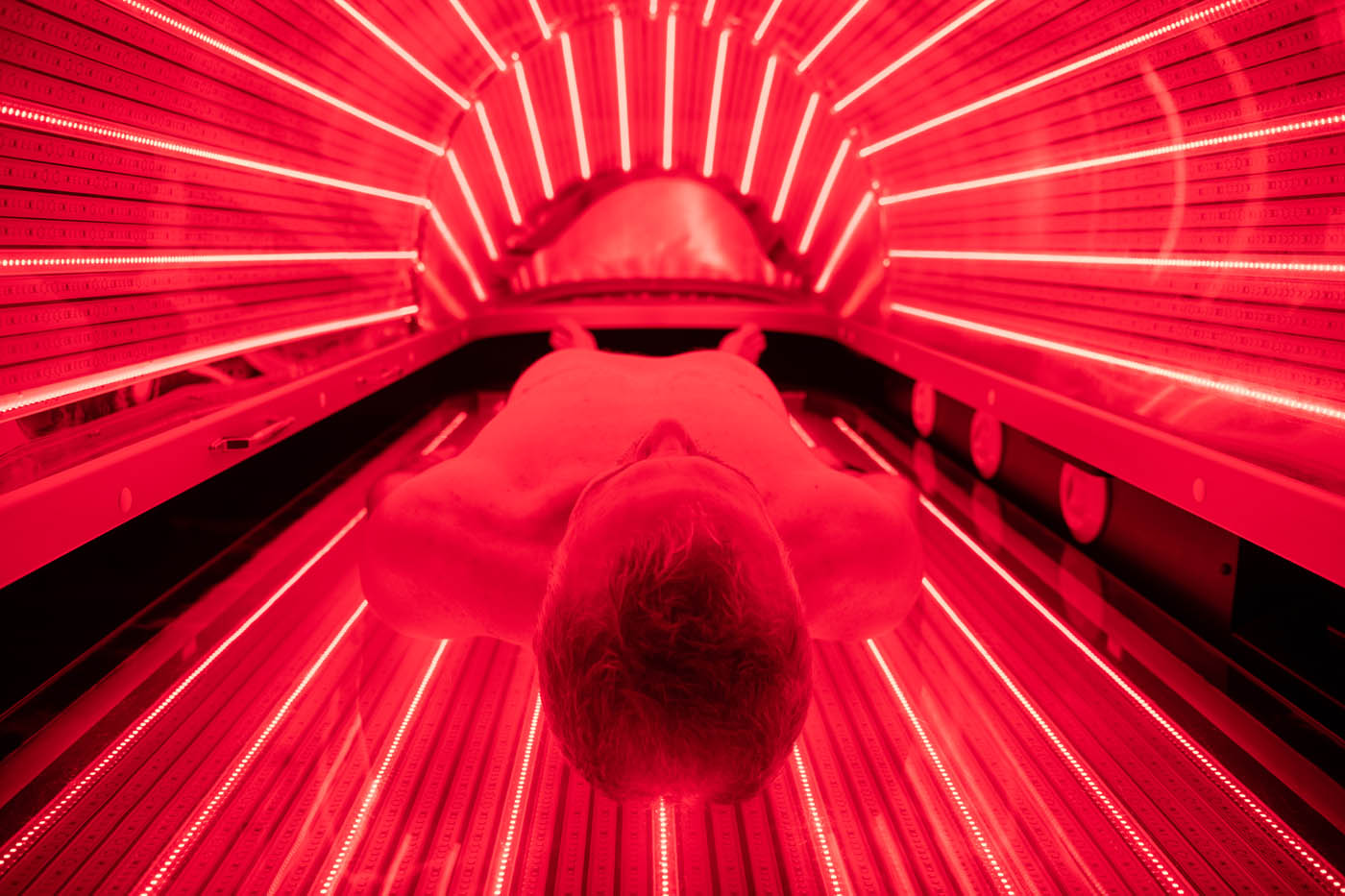 A man getting into a dark pod with bright red light, contact Light Lounge today for your infrared light therapy.