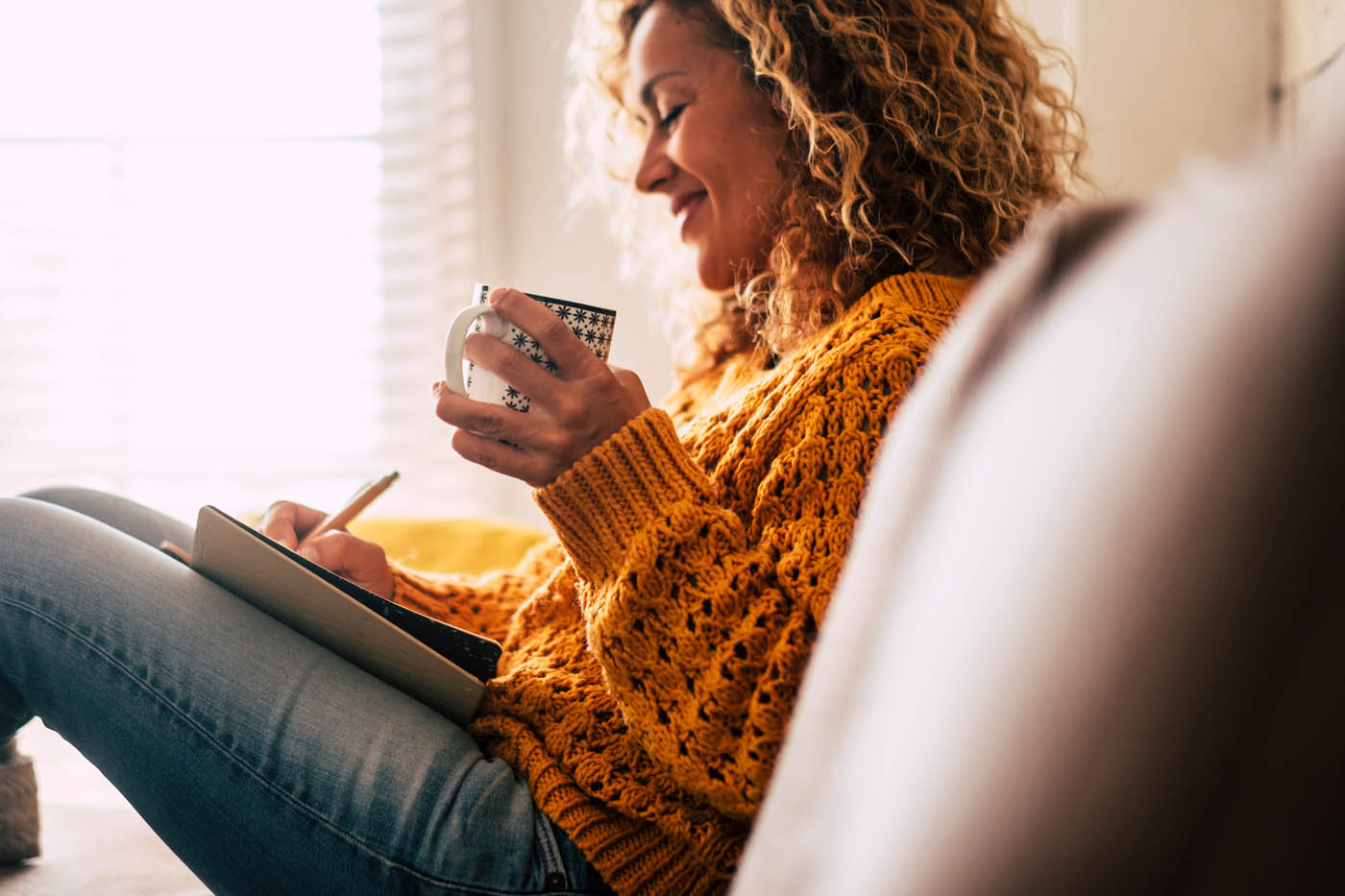 A women with curly hair in an orange sweater enjoying a cup of coffee, book a light therapy appointment with Light Lounge.