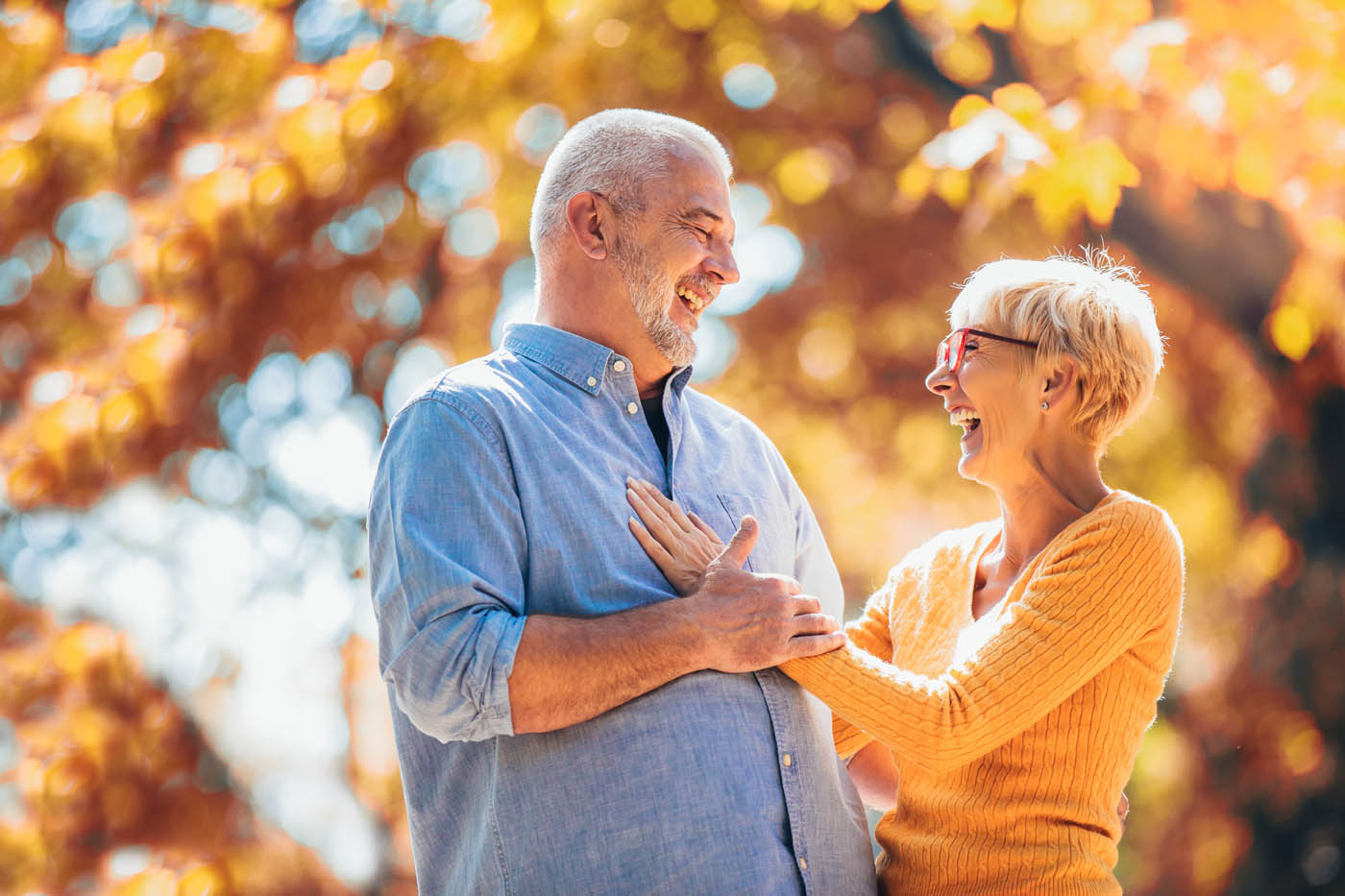 Elderly couple embracing outside in the fall, emjoying the benefits of red light therapy in your local area.